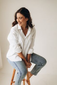 a woman sitting on top of a wooden stool with her legs crossed and looking down