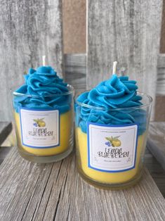 two candles with blue and yellow frosting sitting on top of a wooden table next to each other