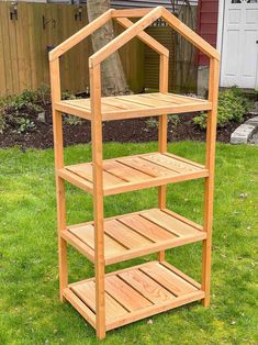 a wooden shelf sitting on top of grass next to a house shaped plant pot holder