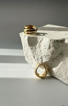 two gold rings sitting on top of a white rock next to a shadowless wall