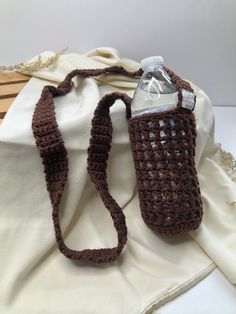 a brown crocheted bag with a water bottle in the middle on a white cloth