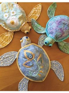 three sea turtles made out of quilts on a wooden table with one turtle looking at the camera