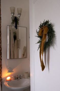 a bathroom with a sink, mirror and wreath hanging on the wall next to it