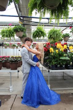 a man and woman standing in front of potted plants with their arms around each other