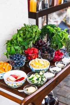 a wooden table topped with bowls of fruit and veggies next to a wall