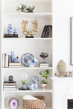 a white bookcase with blue and white vases, books, plants and other decorative items