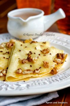 two crepes on a plate with nuts next to a tea cup and saucer