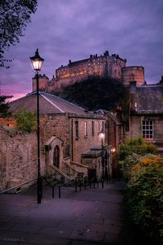 a street light sitting on the side of a road next to a stone building with a castle in the background