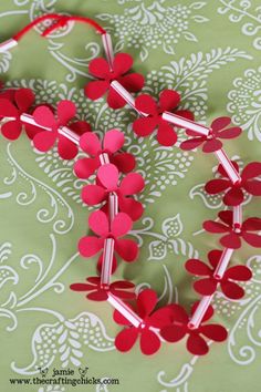 some red paper flowers are on a green and white table cloth with silver pins in the middle