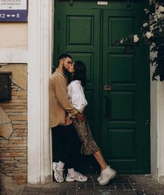 a man and woman kissing in front of a green door