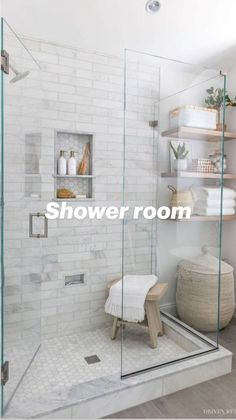 a walk in shower with glass doors and shelves on the wall, along with a stool