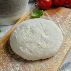 a ball of bread sitting on top of a wooden cutting board next to tomatoes and flour