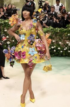 a woman in a yellow dress with flowers on it and cameras around her taking pictures