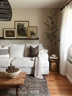 a living room with white couches and pictures on the wall above it's coffee table