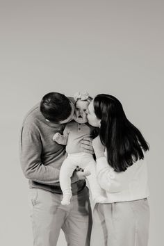 a man and woman kissing their baby while standing next to each other