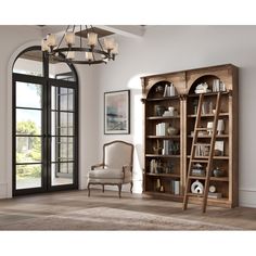 a living room with an open bookcase, chair and chandelier hanging from the ceiling