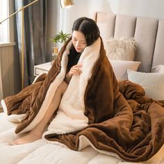 a woman sitting on top of a bed wrapped in a brown and white teddy bear blanket