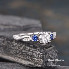 a diamond and blue sapphire ring sitting on top of a rock