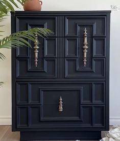 a black dresser with gold handles and knobs next to a potted plant on the floor