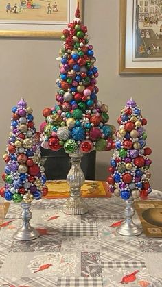 two christmas trees made out of beads sit on a table in front of some pictures