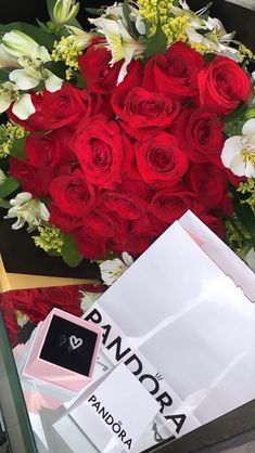 a bouquet of red roses and white lilies in a box next to an unopened diamond ring