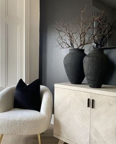 two black vases sitting on top of a wooden cabinet next to a white chair