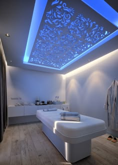 a white bed sitting under a blue light in a bedroom next to a wooden floor