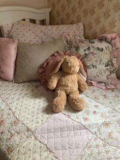 a brown teddy bear sitting on top of a bed next to pillows and pillow cases