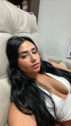 a woman laying on top of a couch next to a white chair with long black hair