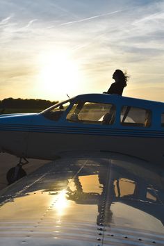 a person sitting on the wing of an airplane at sunset or sunrise, with the sun setting behind them