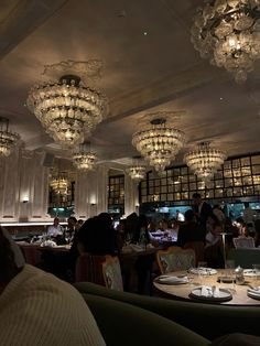 a restaurant with chandeliers hanging from the ceiling and people sitting at tables in front of them