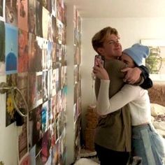 a man and woman taking a selfie in front of a wall with pictures on it