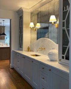 a large kitchen with marble counter tops and white cabinets, along with two lamps on either side of the sink