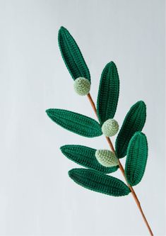 a crocheted green plant with two white balls on it's leaves and stems