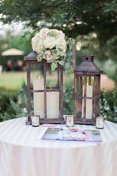 two lanterns are sitting on top of a table with flowers and candles in them,