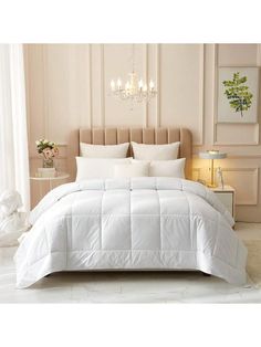 a bed with white comforter and pillows in a room next to a chandelier