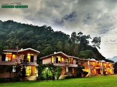 two large houses with lights on in front of a green hillside and dark cloudy sky