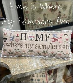 a cross stitch pillow sitting on top of a wooden bench with the words home is where my samples are