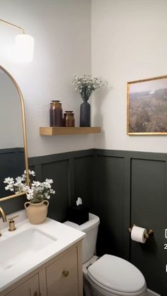 a white toilet sitting next to a bathroom sink under a framed picture on the wall