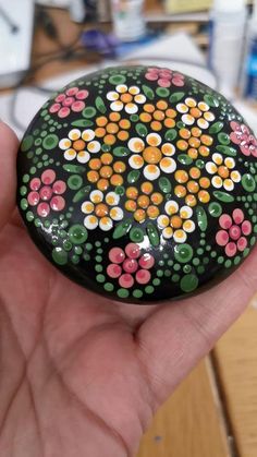 a hand holding a painted rock with flowers on it