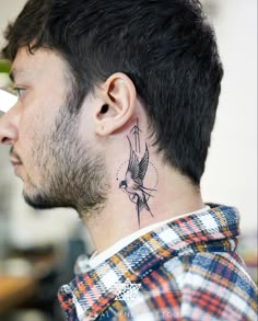 a man with a bird tattoo on his neck and behind his ear, looking to the side