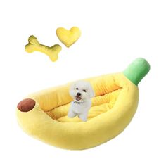 a small white dog sitting in a banana shaped bed next to two yellow dogs toys