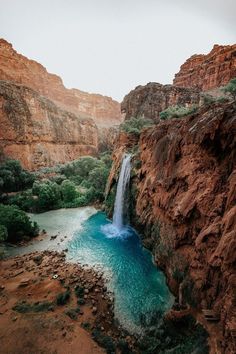 a waterfall in the middle of a canyon with blue water running down it's side