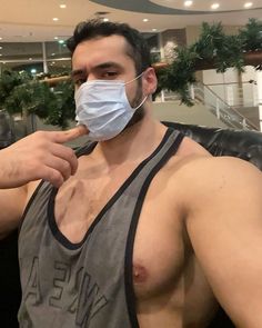 a shirtless man wearing a face mask and looking at the camera while brushing his teeth