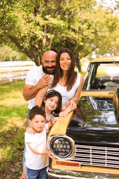 a man, woman and two children standing in front of a car