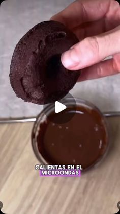 a person holding a chocolate cookie in front of a bowl of melted chocolate on a table