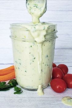 a jar filled with dressing next to carrots and tomatoes