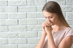 a woman with her hands clasped to her chest, standing in front of a brick wall