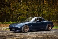 a blue car parked on top of a dirt road next to trees and grass in the background