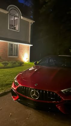 a red sports car parked in front of a house at night with its lights on